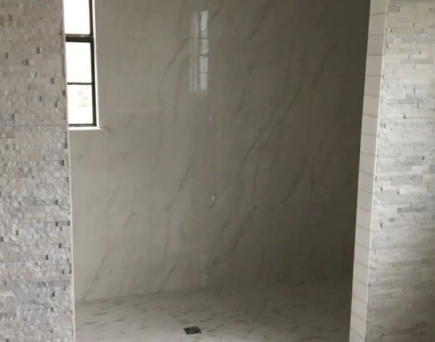 Arched walk-in shower with marble-look wall tile and a textured stone surround.