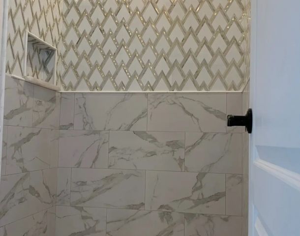 Geometric mosaic shower with marble-look wall tile and a pebble mosaic floor.