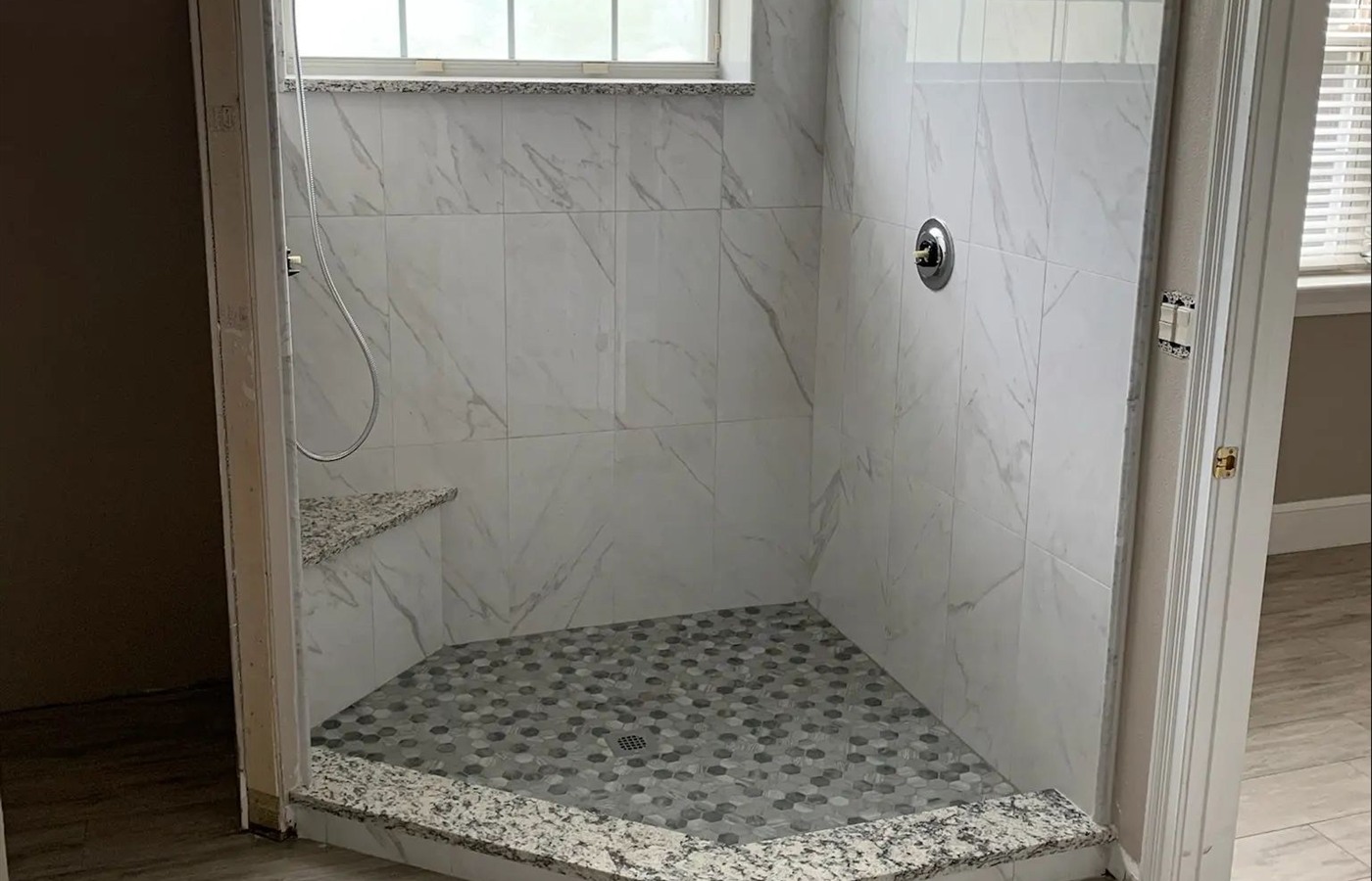 Compact marble-look shower with a dark pebble mosaic floor and polished stone curb.