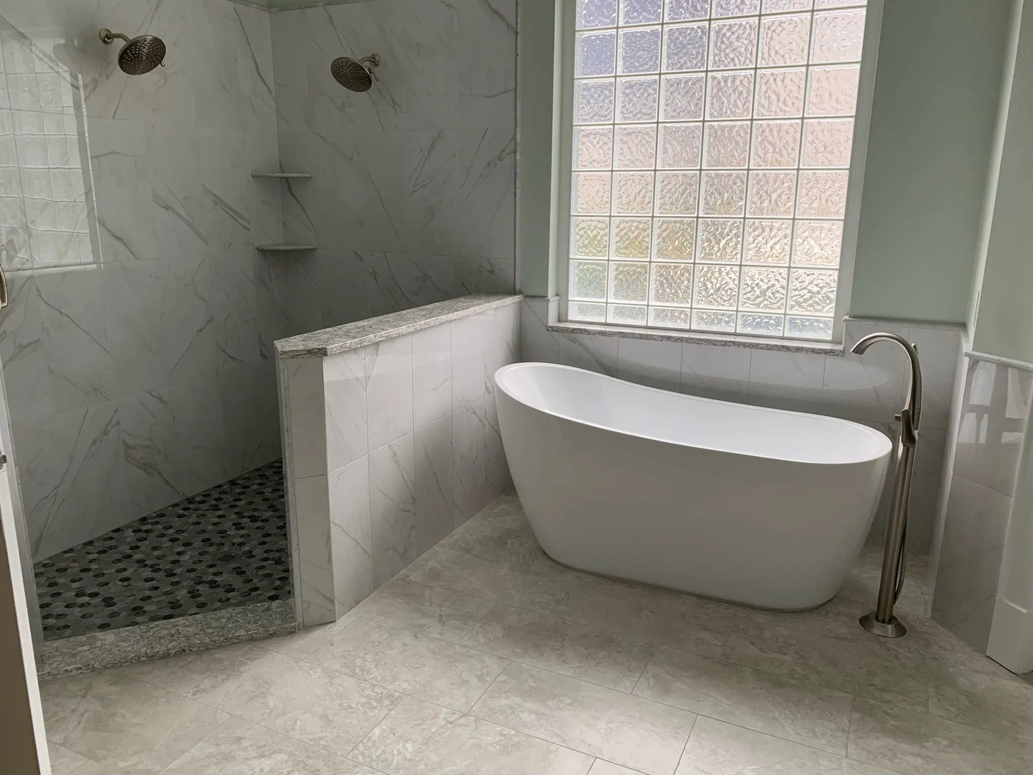 Wide view of a freestanding tub beside an open marble-look shower and pebble floor.