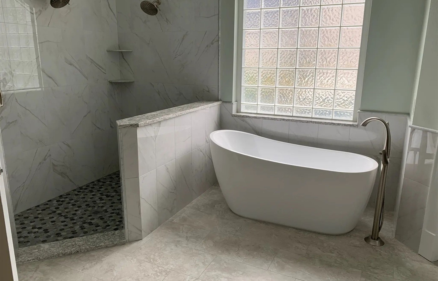 Freestanding tub beside a marble-look walk-in shower with a pebble mosaic floor.