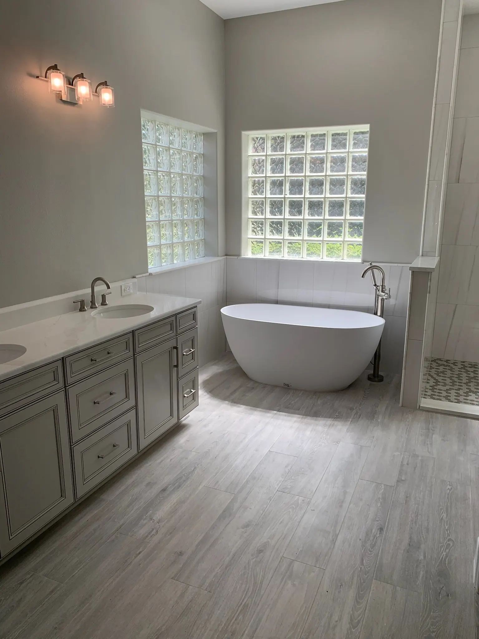 Bright bathroom with gray vanity, freestanding tub, glass block windows, and tiled shower.