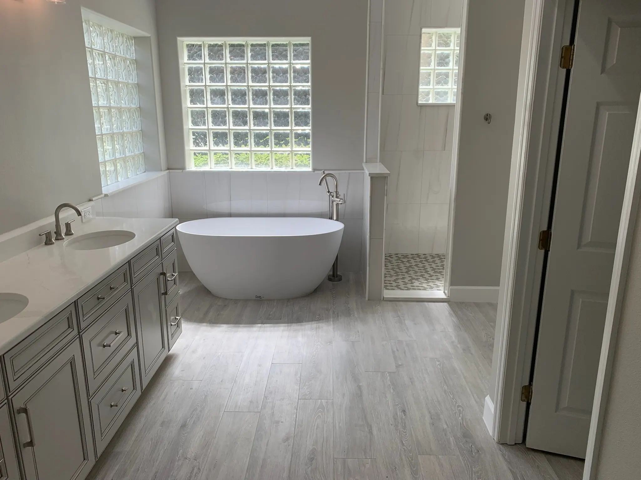 Wide modern bathroom with double vanity, freestanding tub, glass block windows, and shower.