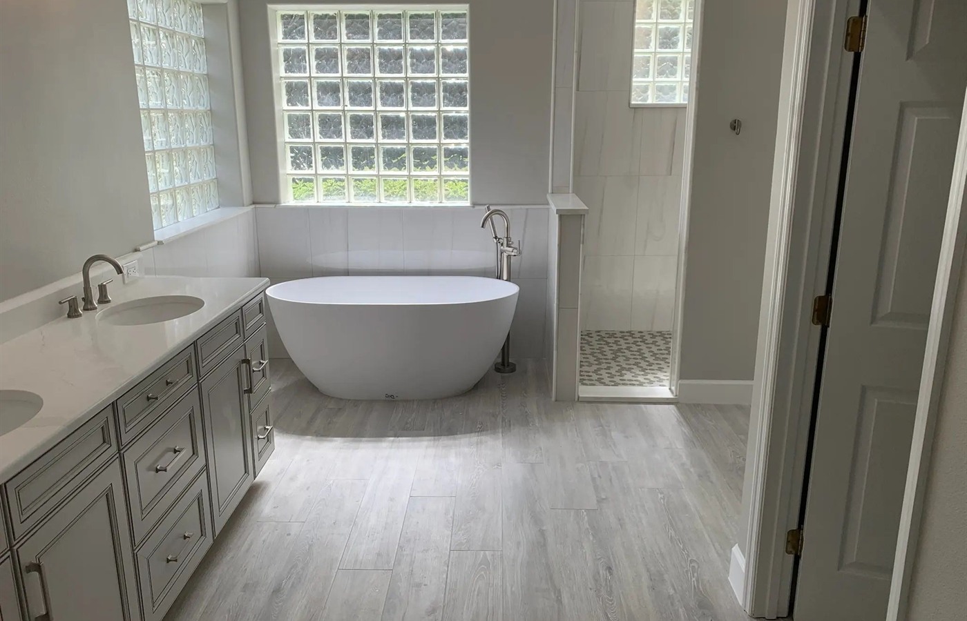 Modern bathroom with glass block windows, freestanding tub, gray vanity, and tiled shower.