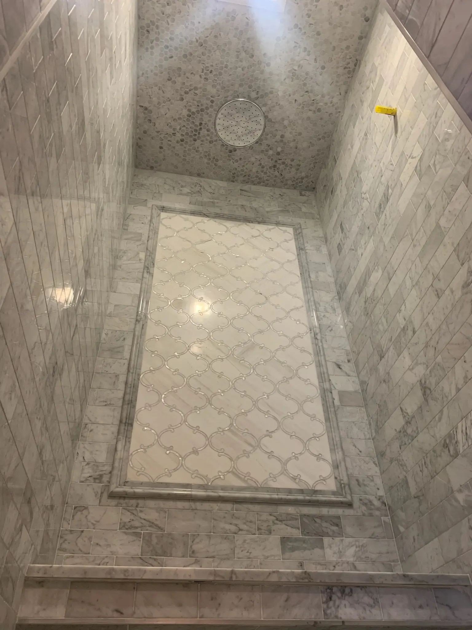 Gray marble shower with mosaic ceiling, framed accent panel, and stone bench.