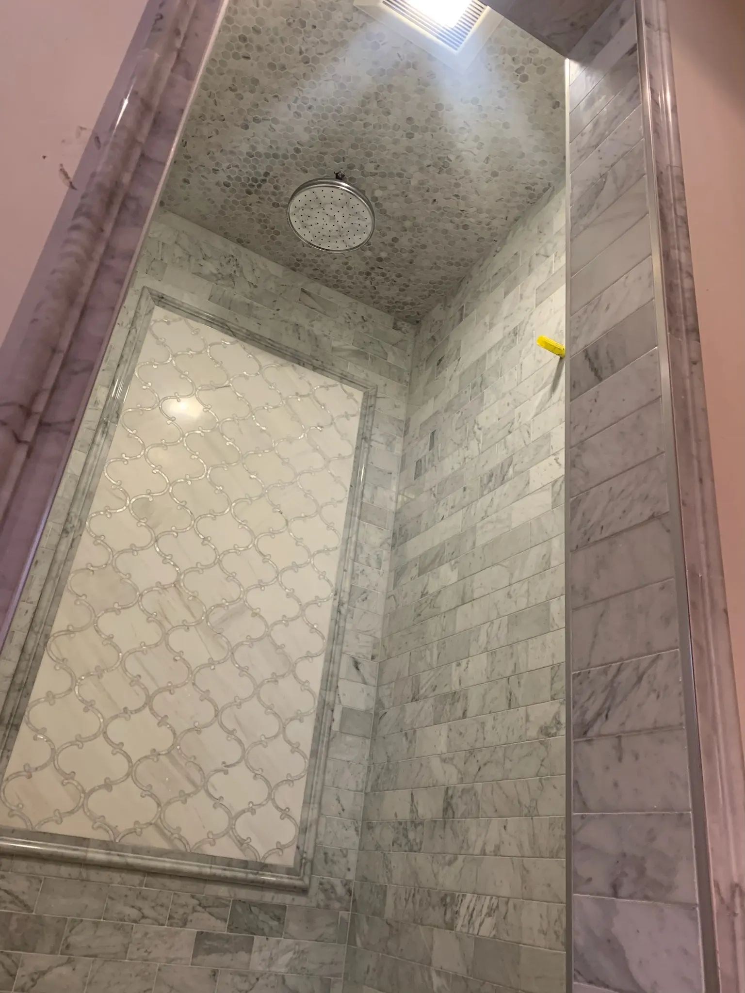 Angled view upward inside a gray marble shower with patterned ceiling tile.