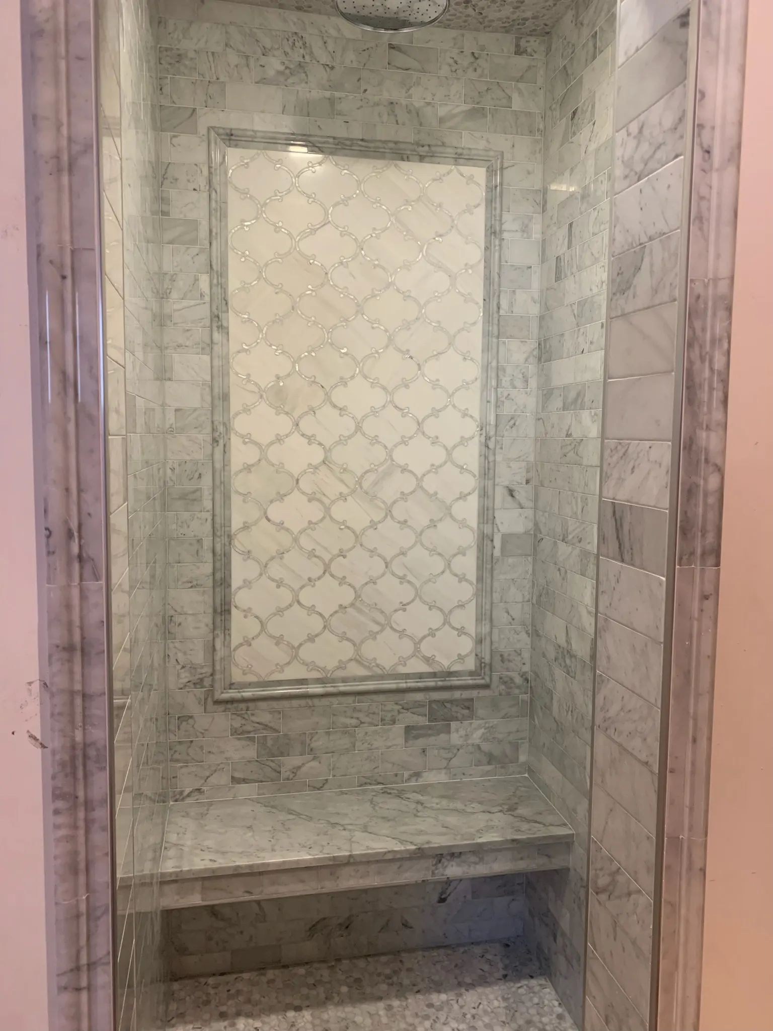 Framed patterned accent panel above a substantial gray stone shower bench.