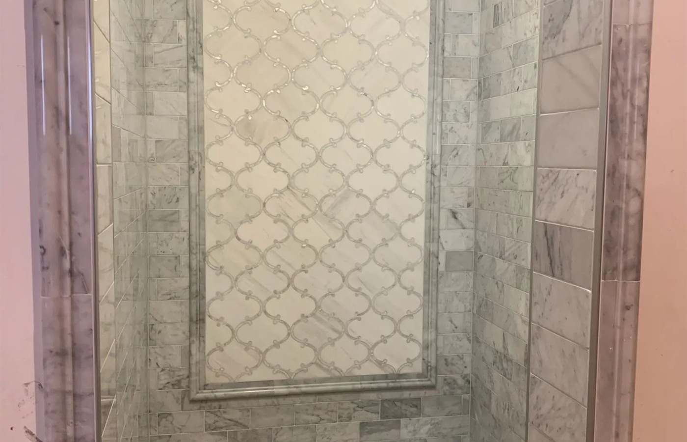 Gray marble shower with a framed patterned accent panel and stone bench.