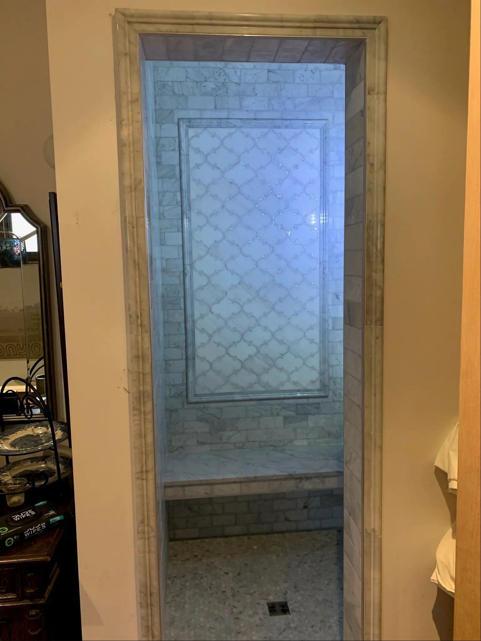 Doorway view into a gray marble shower with a built-in bench and framed window panel.