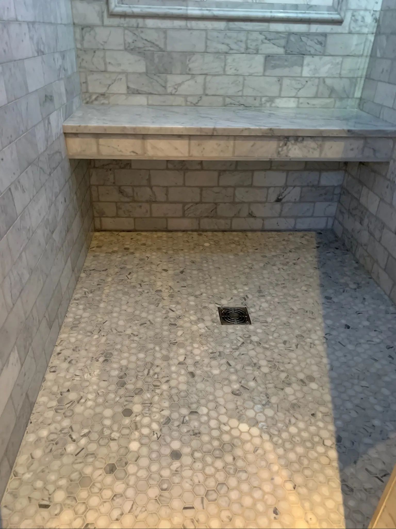 Built-in gray tile shower bench above a penny mosaic floor.