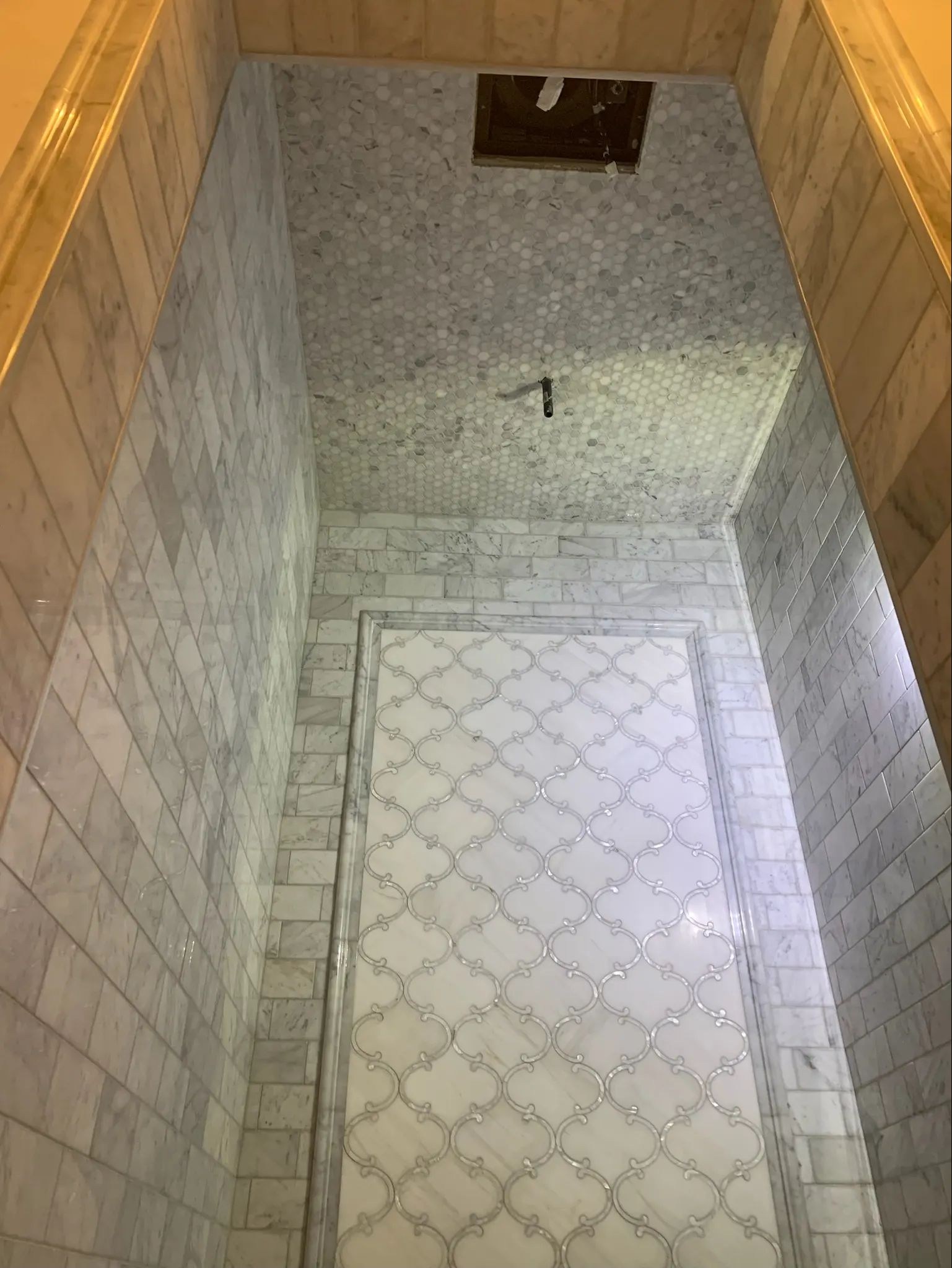 View upward to a mosaic shower ceiling above gray marble walls.