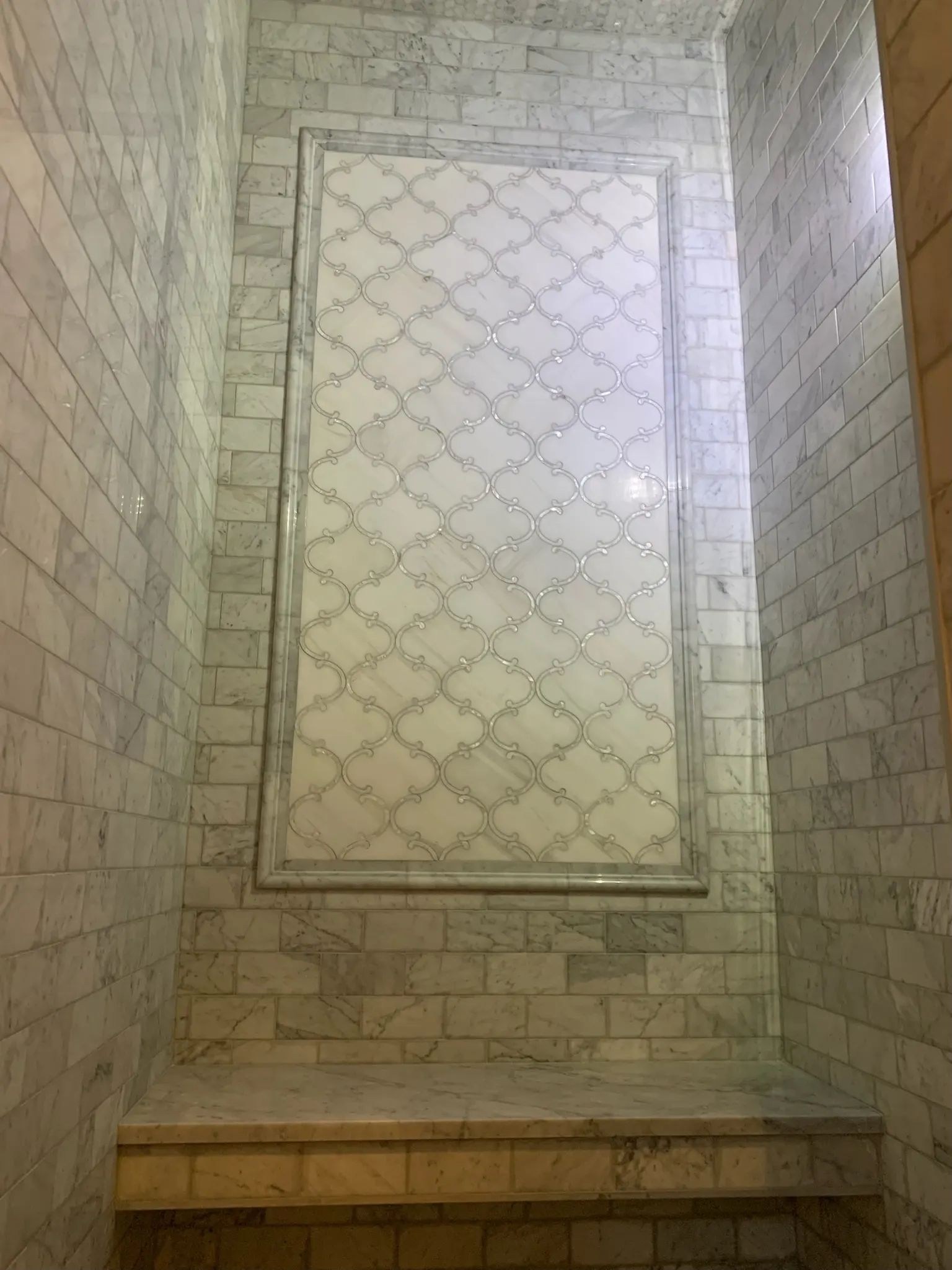Framed decorative window panel centered above a gray tiled shower bench.