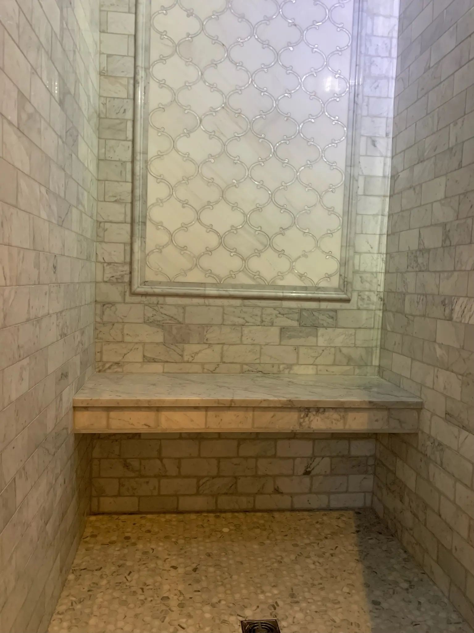 Full shower bench wall with gray marble tile, framed window panel, and penny mosaic floor.