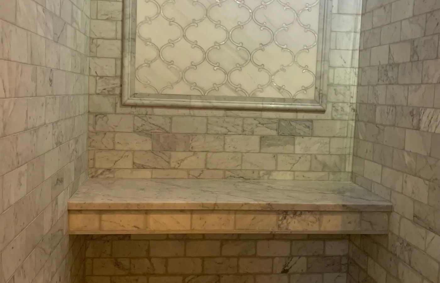 Gray marble-tiled shower with a built-in bench, framed window panel, and penny mosaic floor.