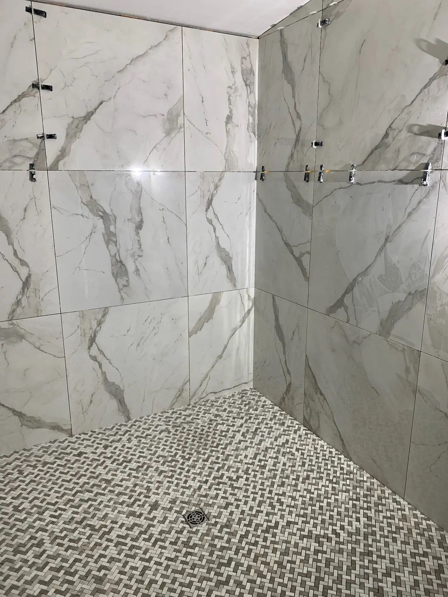 Large marble-look tile shower with dramatic veining and a patterned mosaic floor.