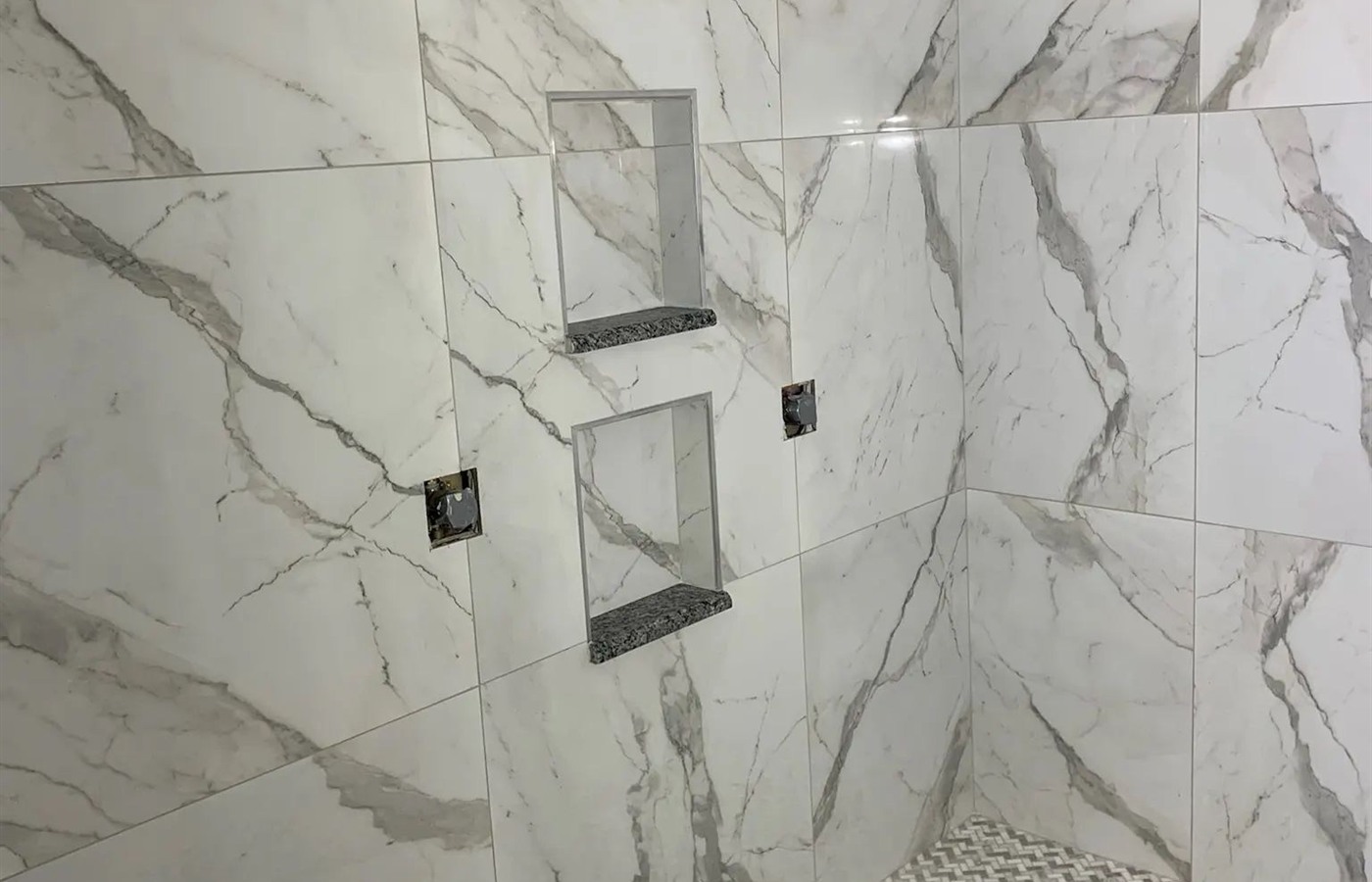 Large-format marble-look shower with recessed niches and a basketweave mosaic floor.