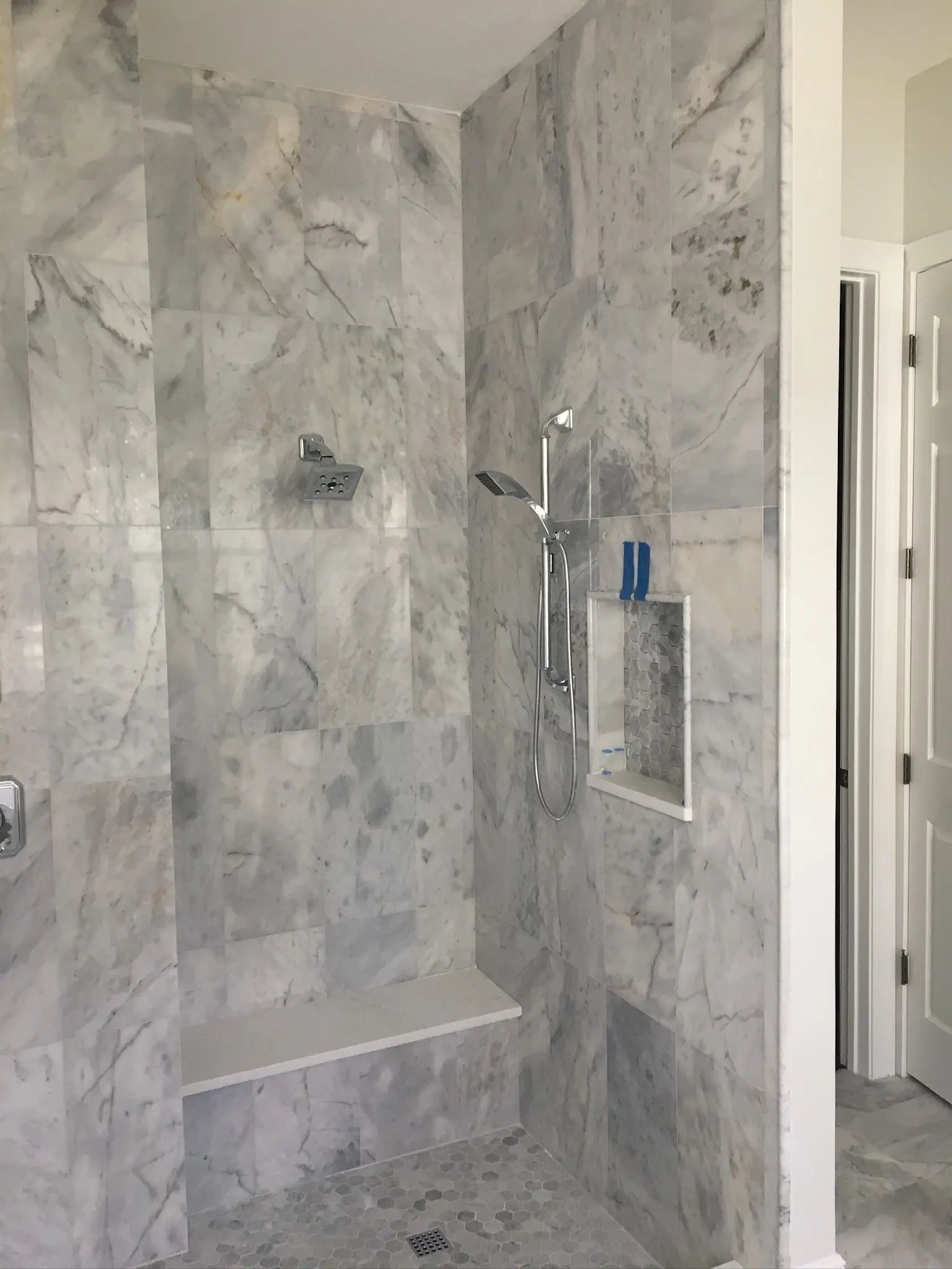 Wide view of a gray marble walk-in shower with bench, niche, and mosaic flooring.