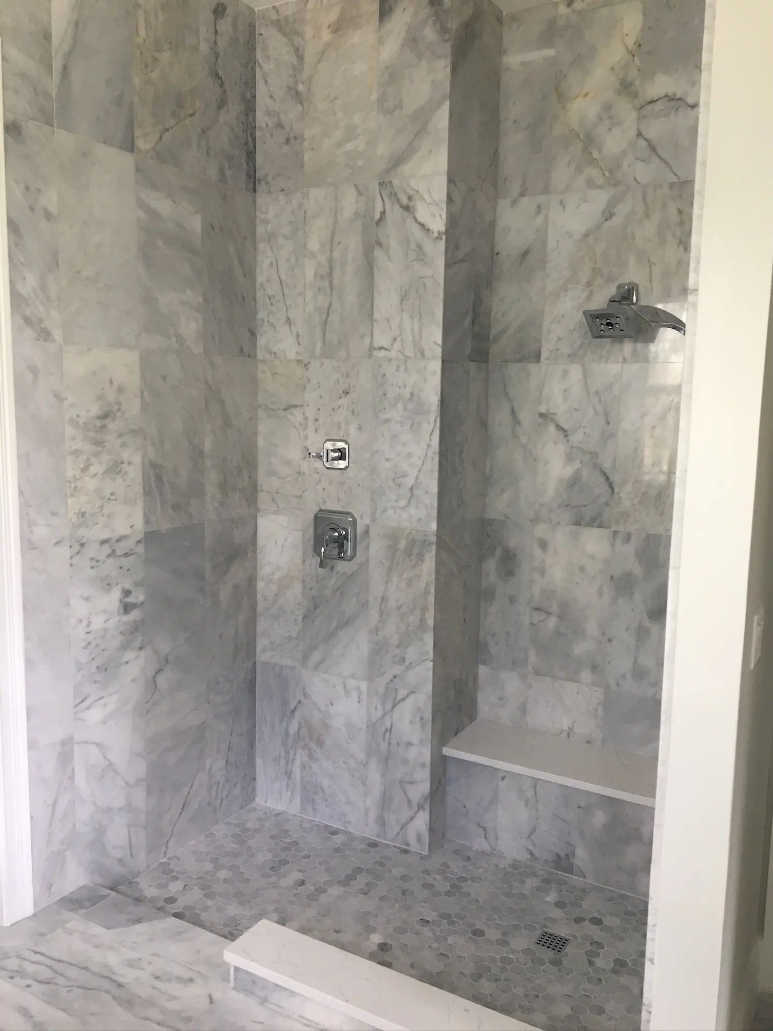 Gray marble shower interior with wall-mounted fixtures, recessed niche, and built-in bench.