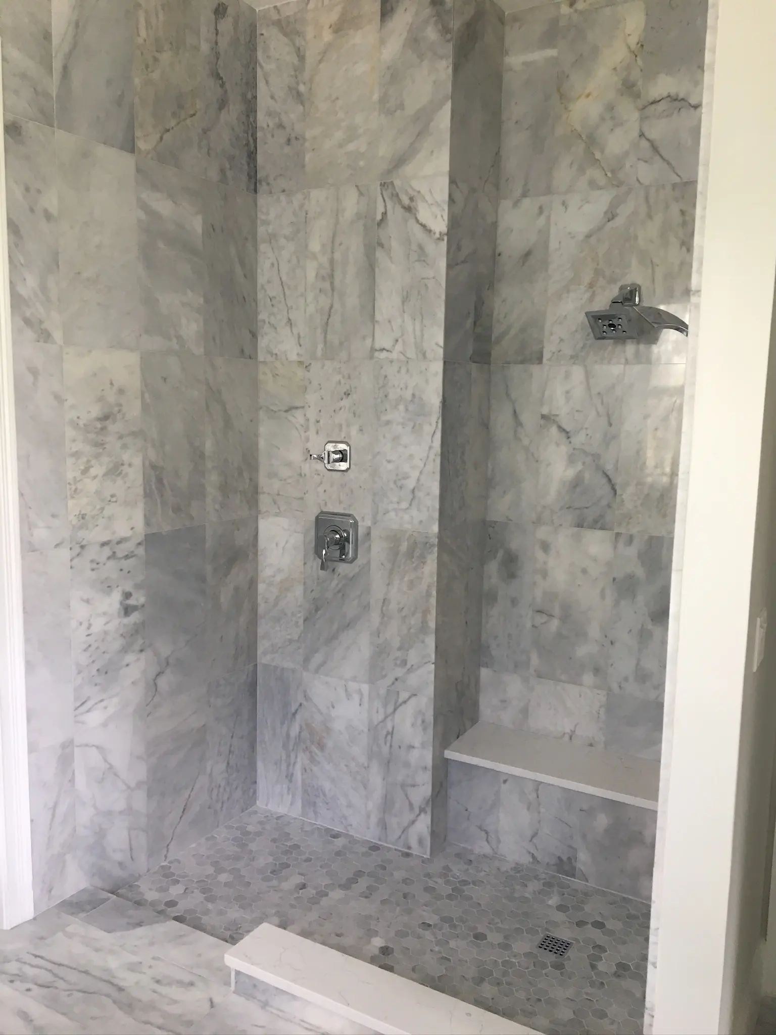 Angled view into a marble-tiled walk-in shower with a bench and mosaic floor.
