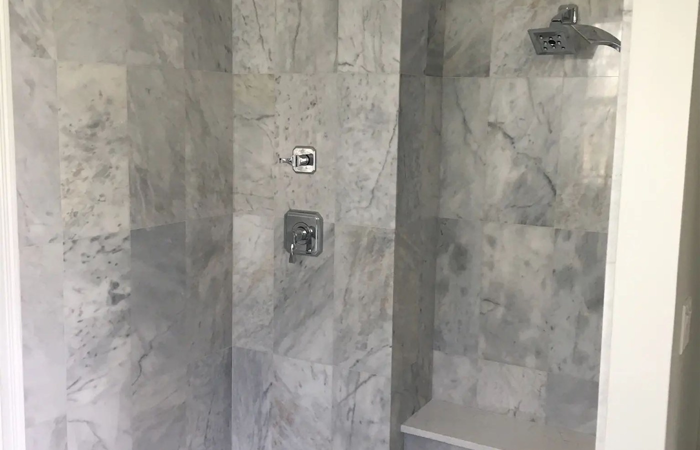 Gray marble walk-in shower with a built-in bench, recessed niche, and mosaic floor.