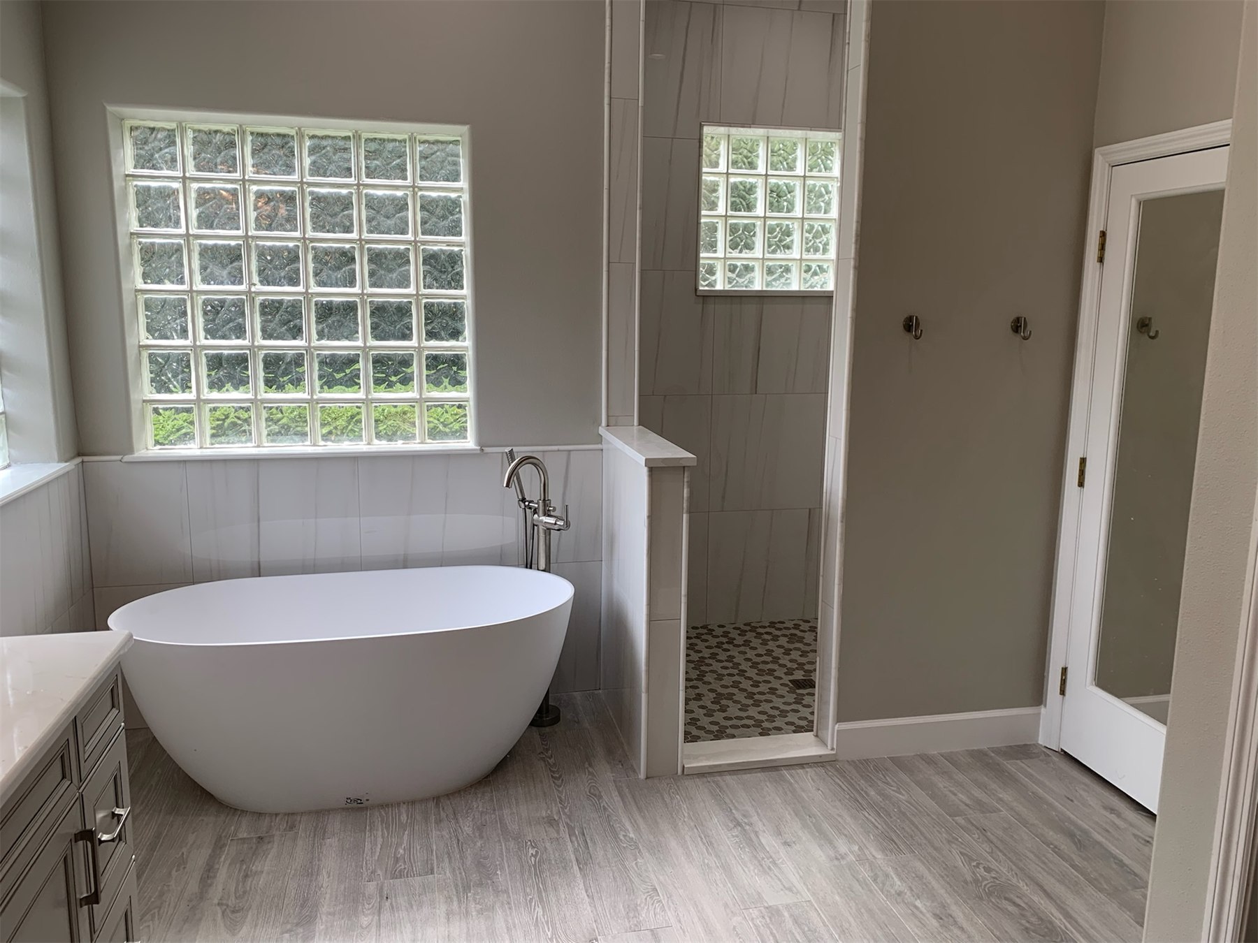 Bathroom remodel with a freestanding tub, tiled walk-in shower, glass block windows, and wood-look floor tile.