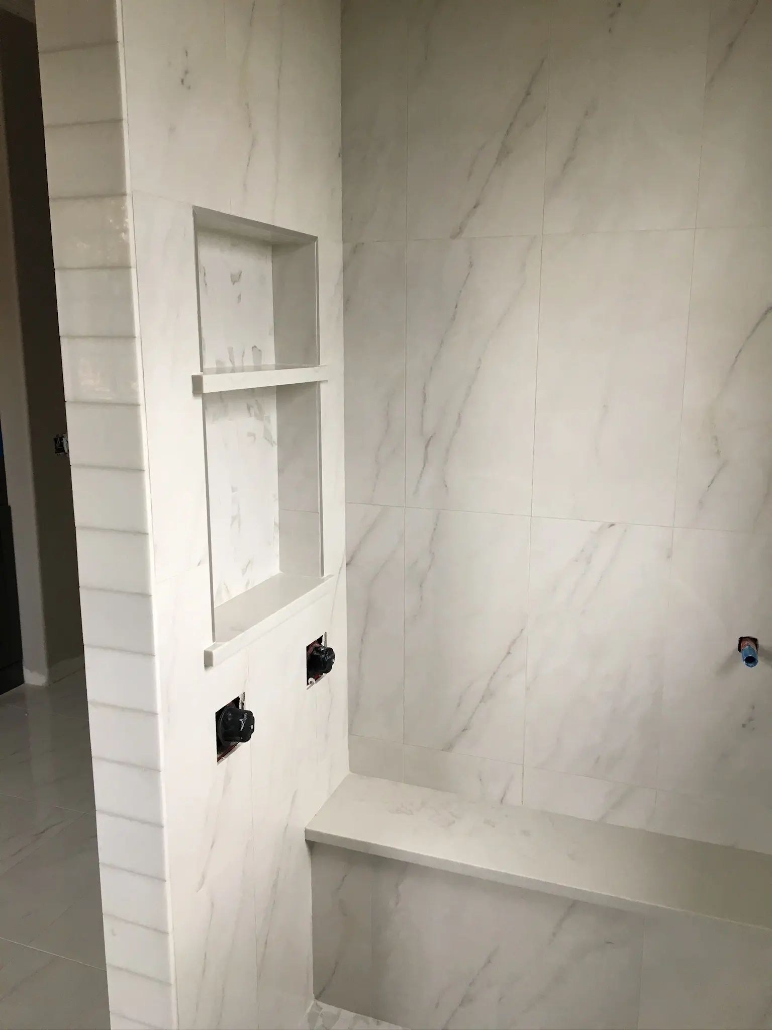 Marble-look shower interior with a recessed niche, tiled bench, and clean wall transitions.