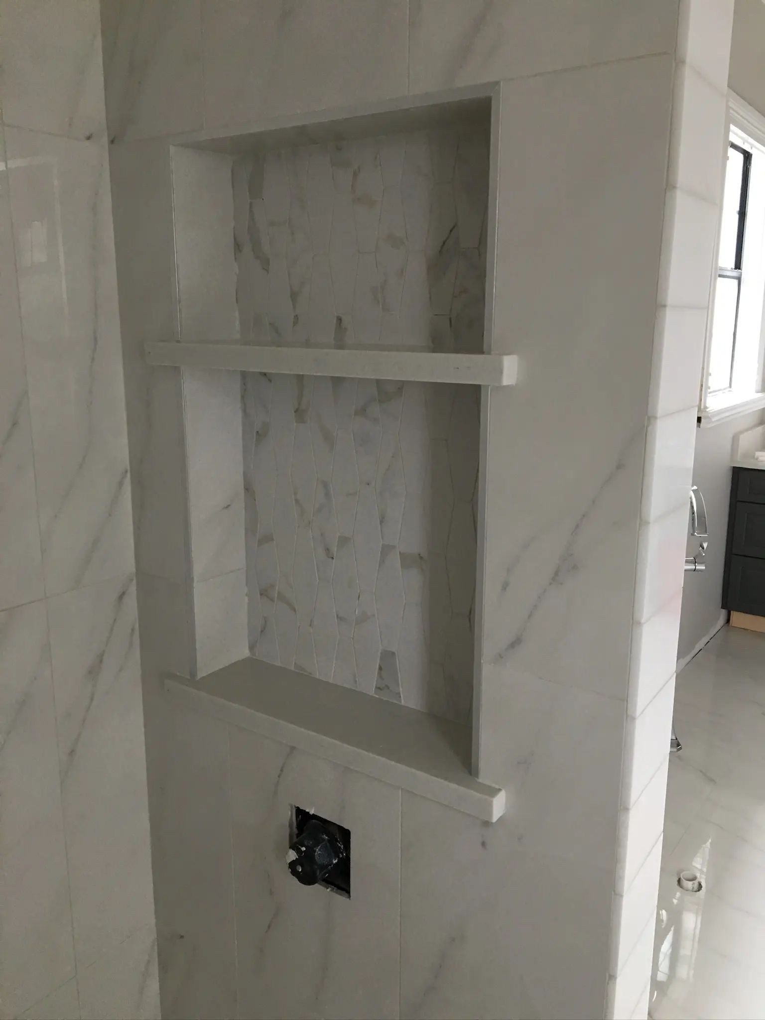 Recessed shower shelving integrated into a marble-look tiled partition wall.