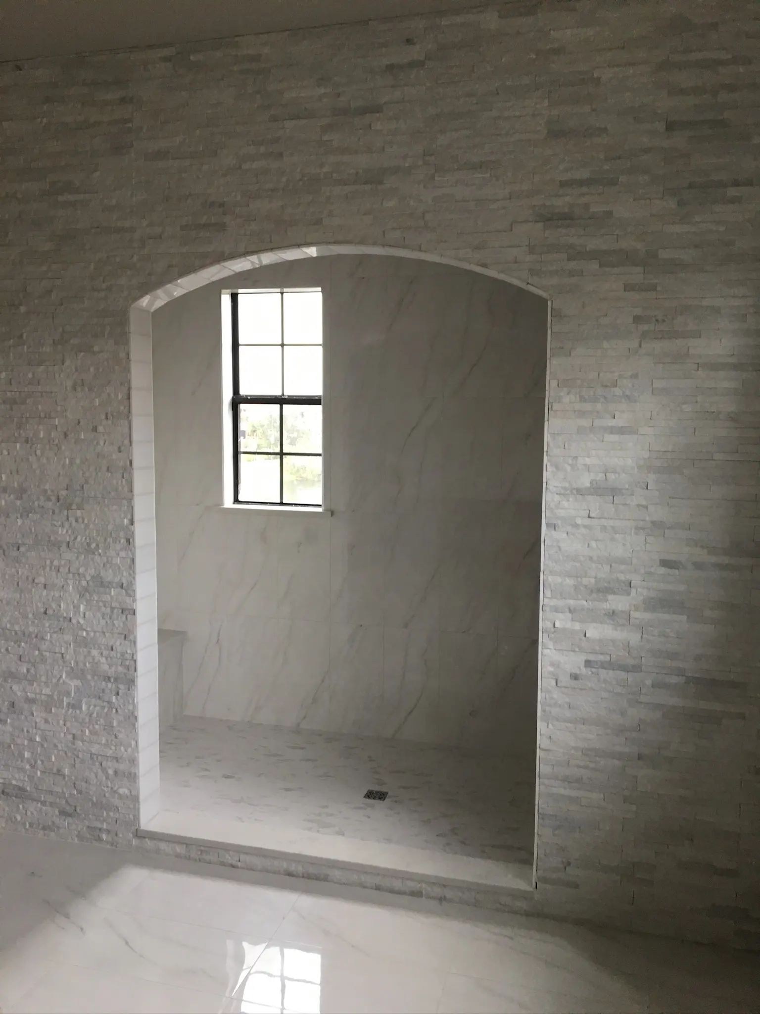 Arched shower opening framed with textured stone tile around a bright marble-look interior.