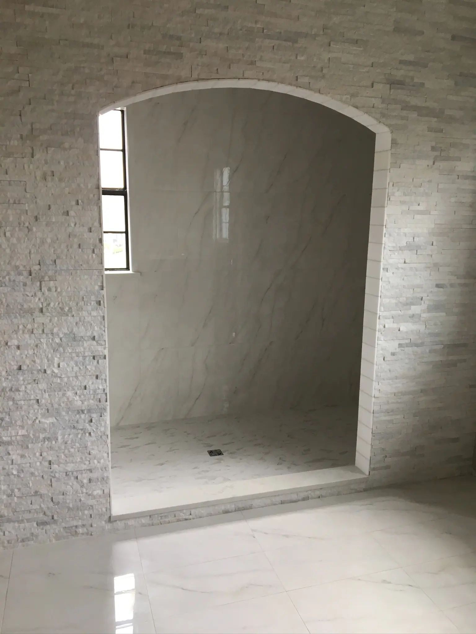Full arched walk-in shower entry with textured stone surround and marble-look tile.