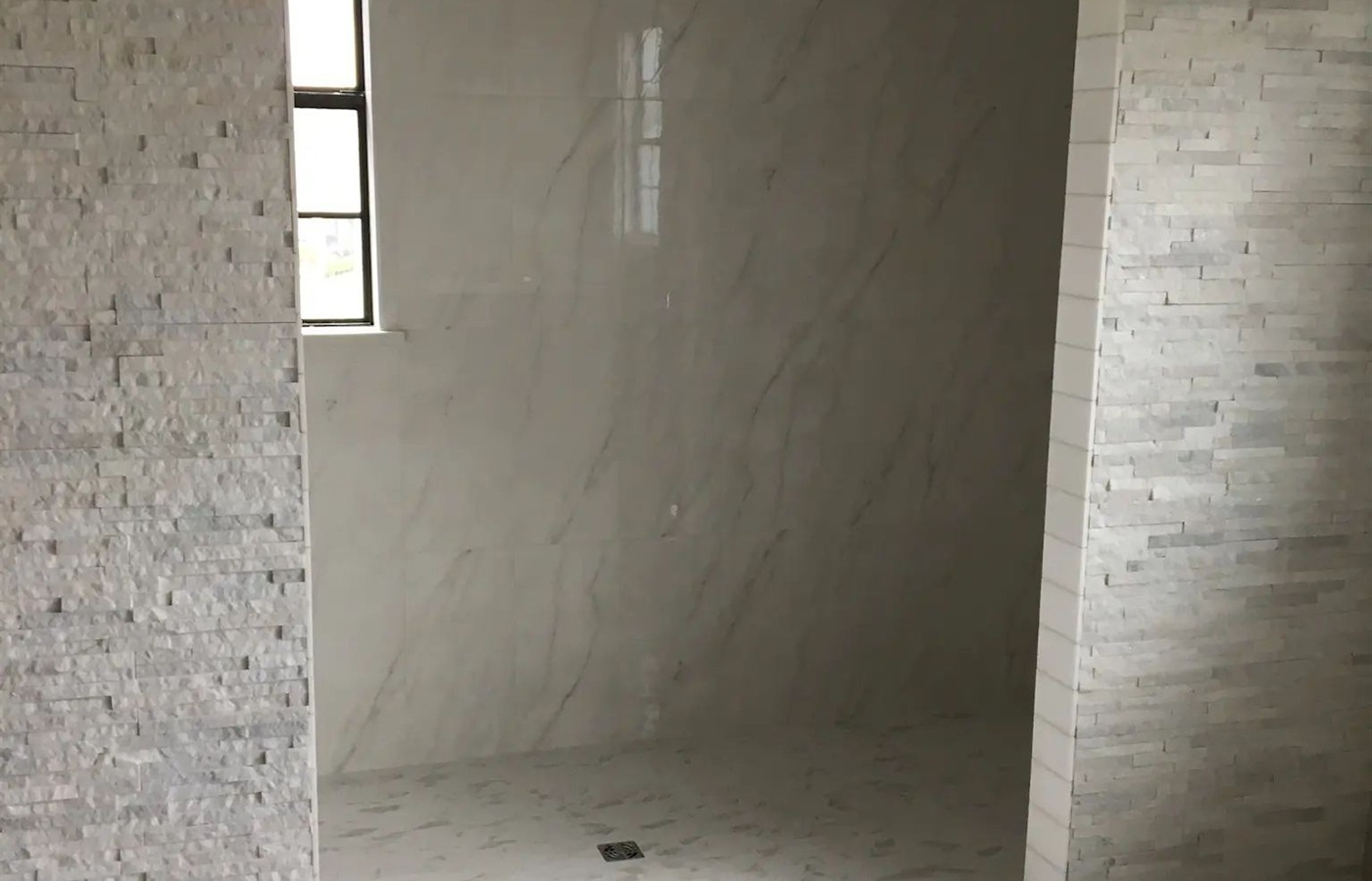 Arched walk-in shower with marble-look wall tile and a textured stone surround.