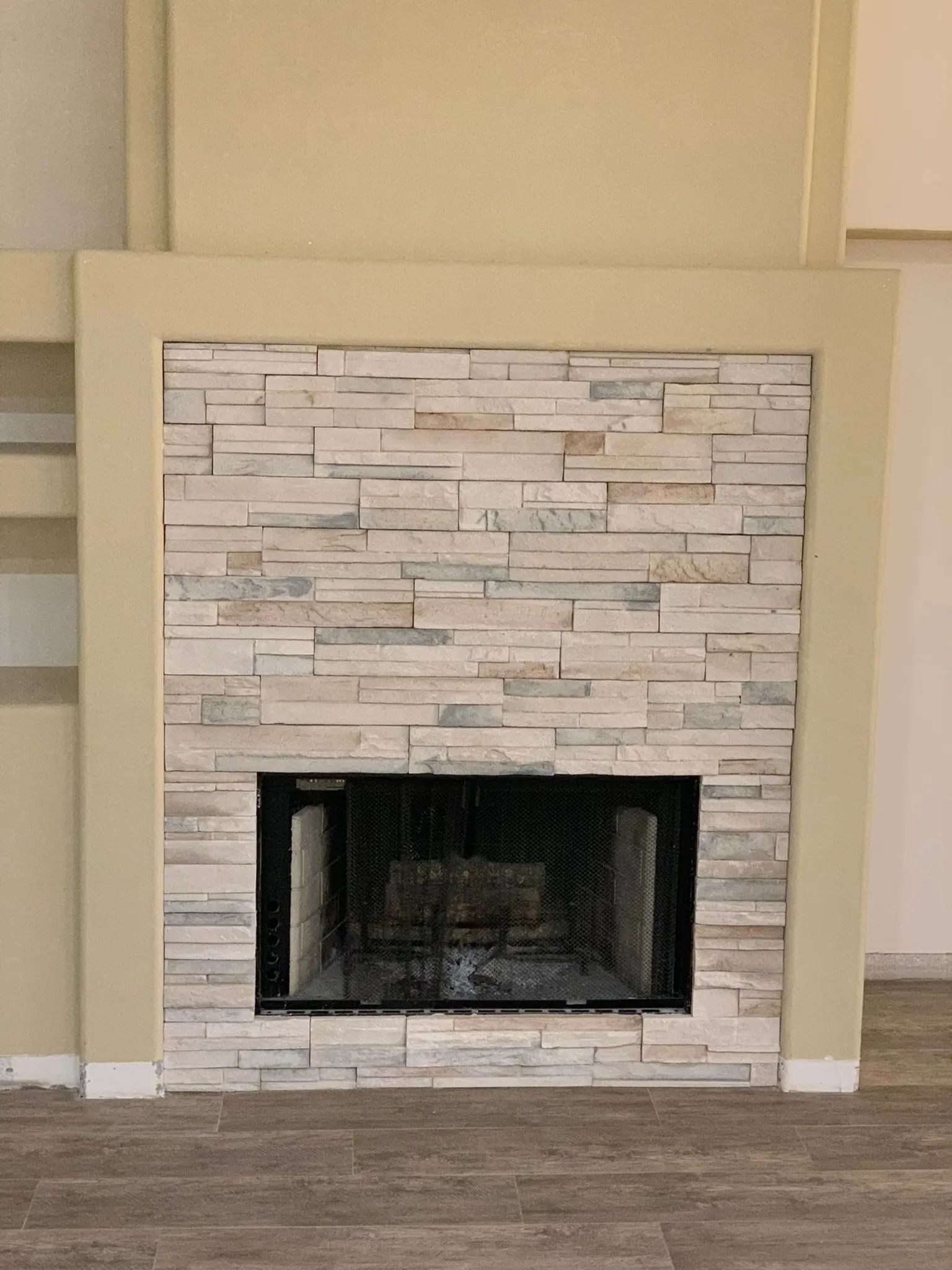 Close view of a fireplace faced with light neutral stacked stone and a slim flush hearth.