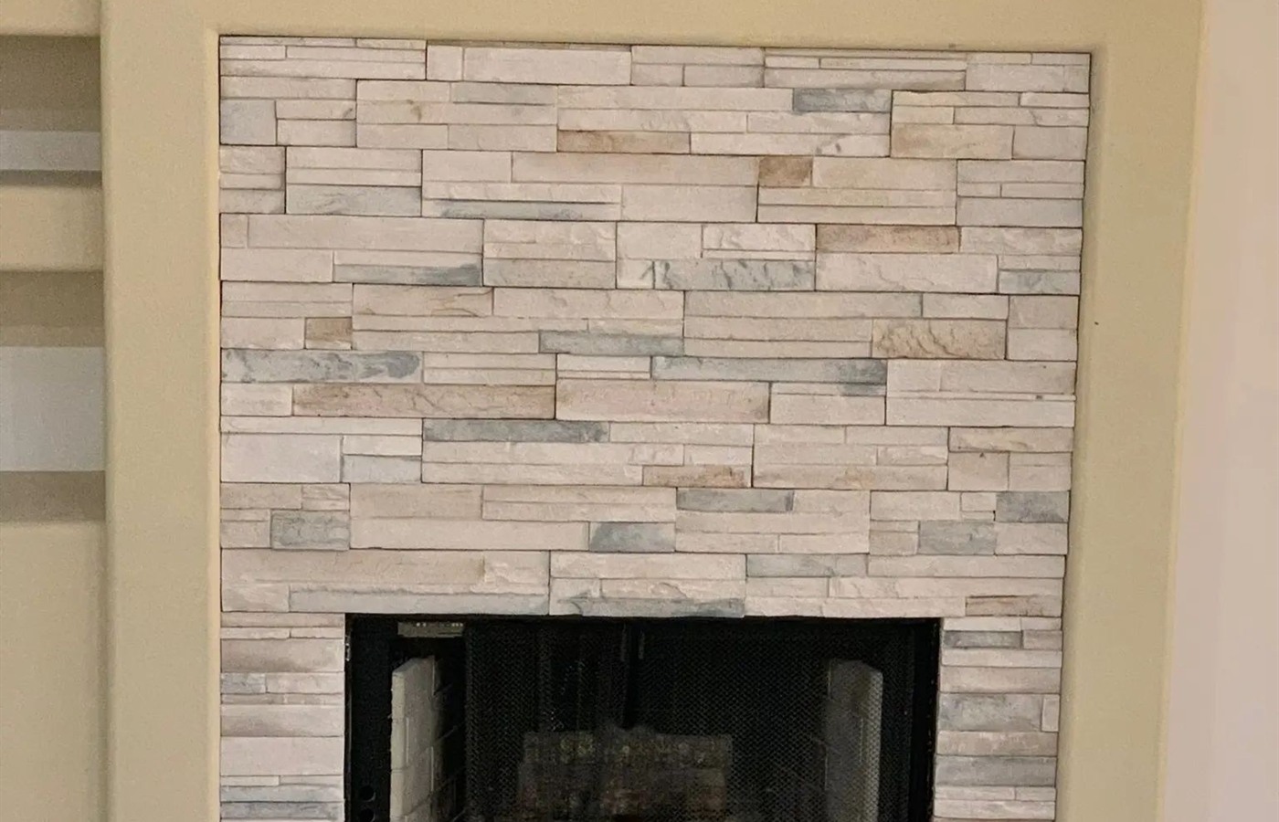 Modern fireplace faced with neutral stacked stone veneer and a flush hearth.