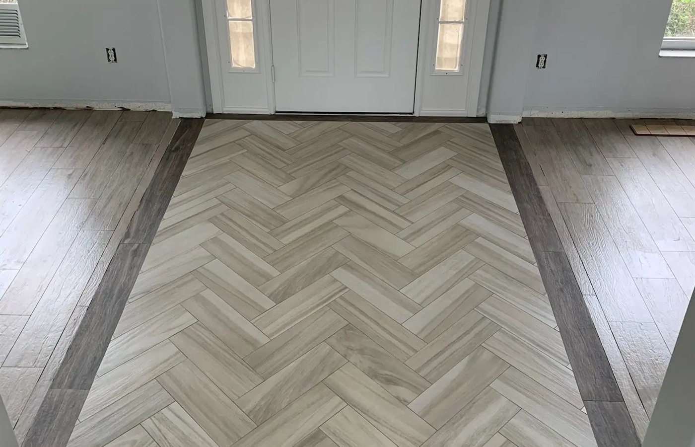 Herringbone tile entry inset framed by a dark border and wood-look plank flooring.