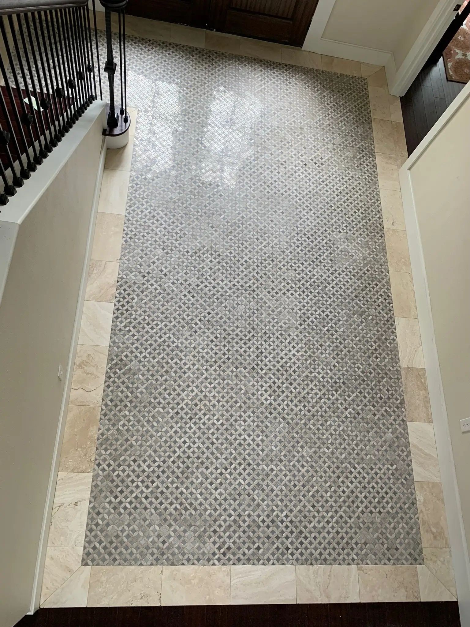 Long hallway floor with a gray geometric mosaic field and wide marble-look tile border.