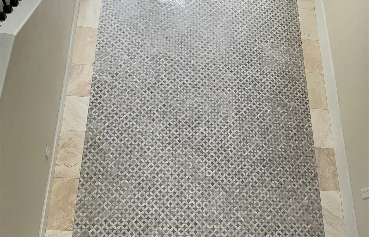 Geometric mosaic tile hallway floor framed by a wide marble-look border.
