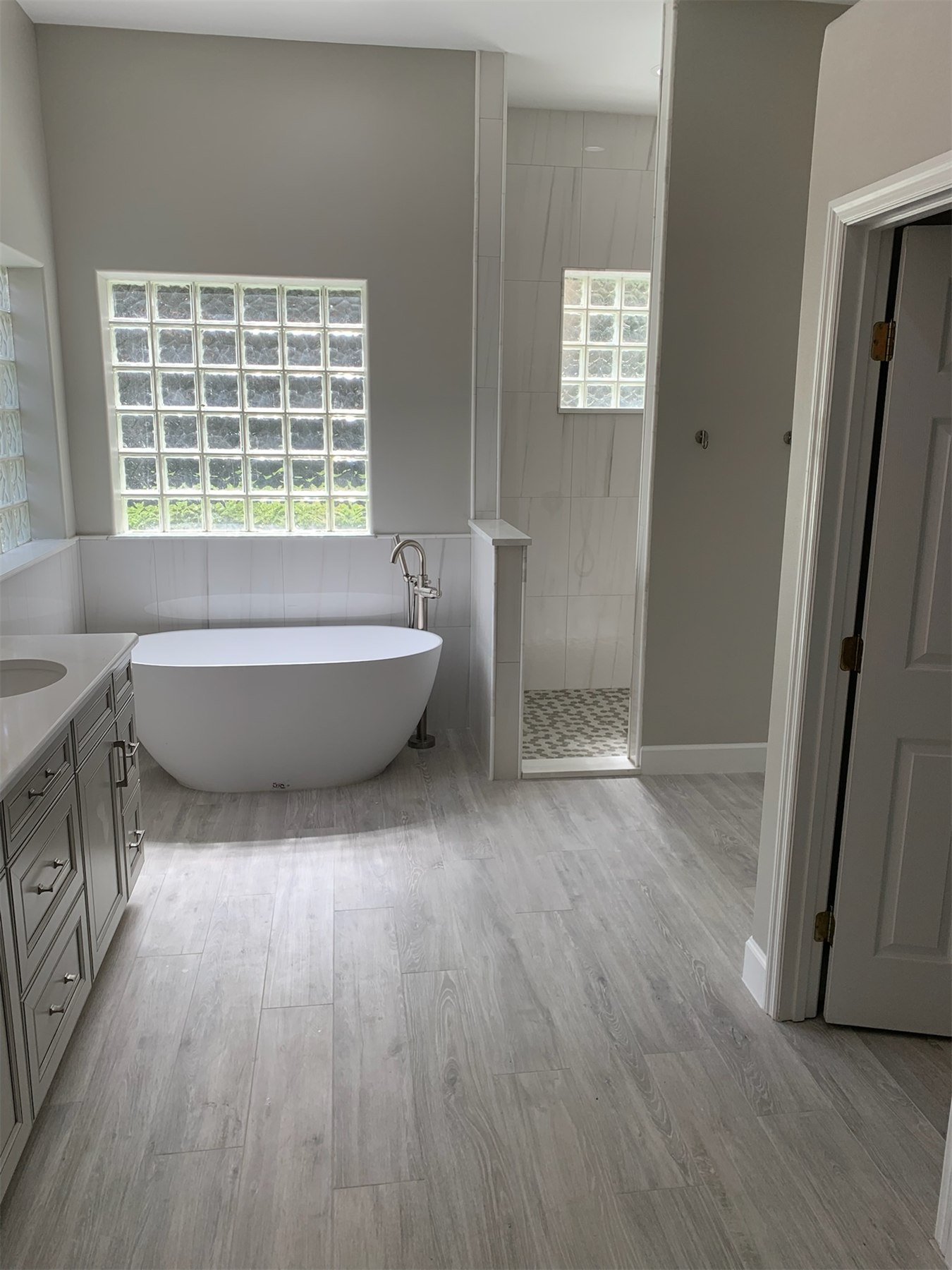 Freestanding tub beneath glass block windows beside a marble-look tiled walk-in shower.