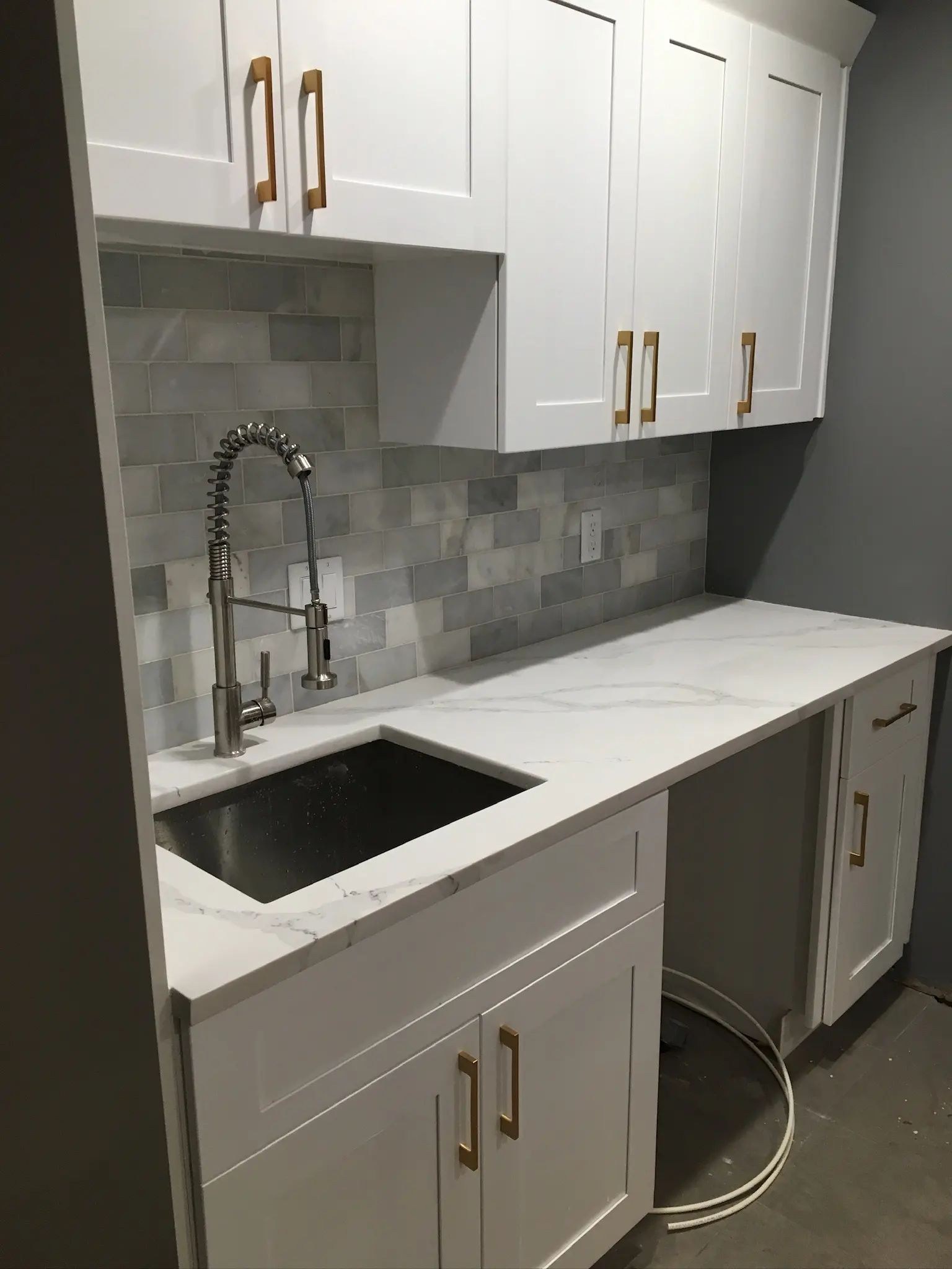 White sink cabinet area with a gray marble-look tile backsplash and gold hardware.