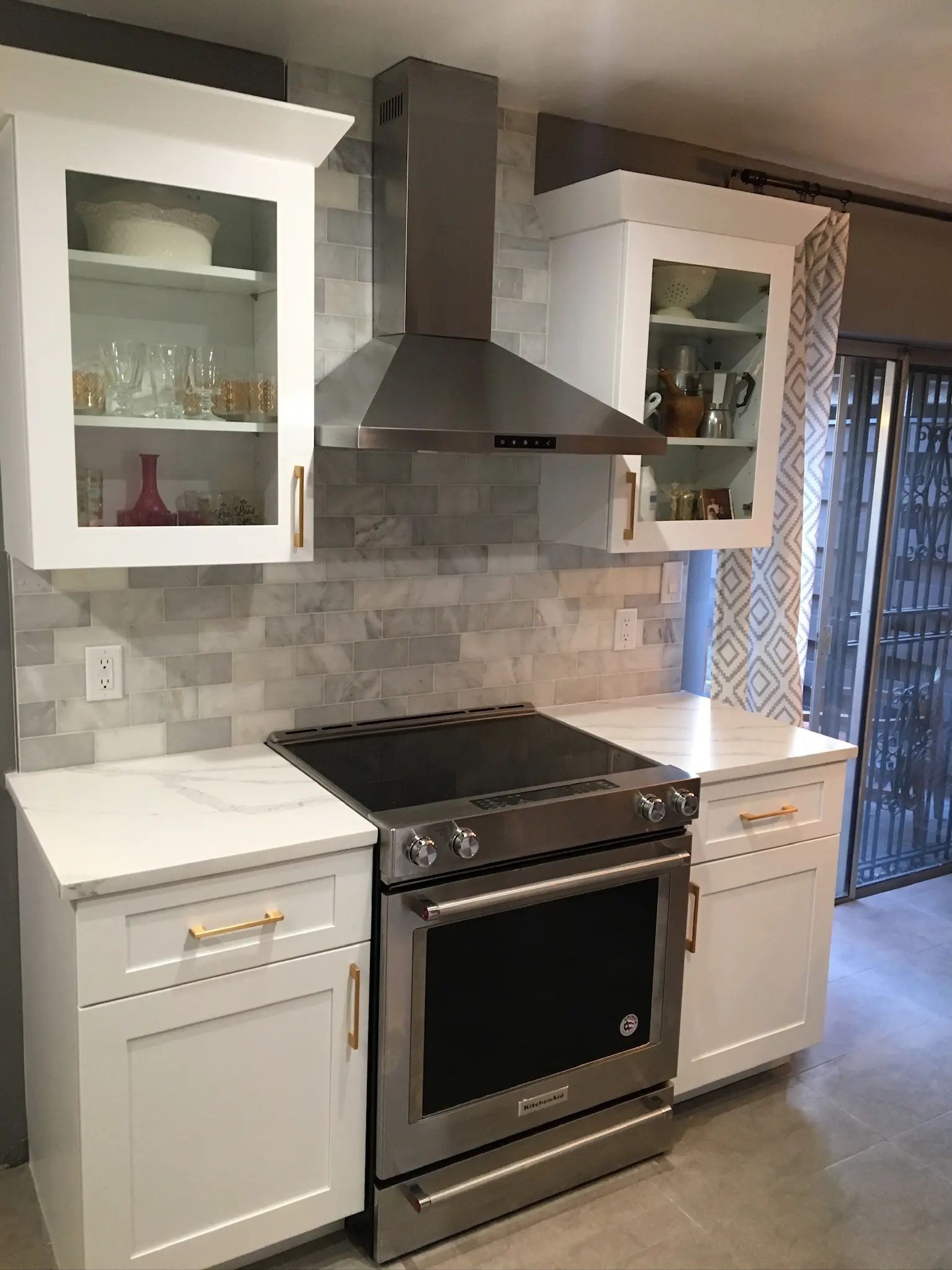 White kitchen range wall with gray marble-look backsplash tile and glass-front cabinets.