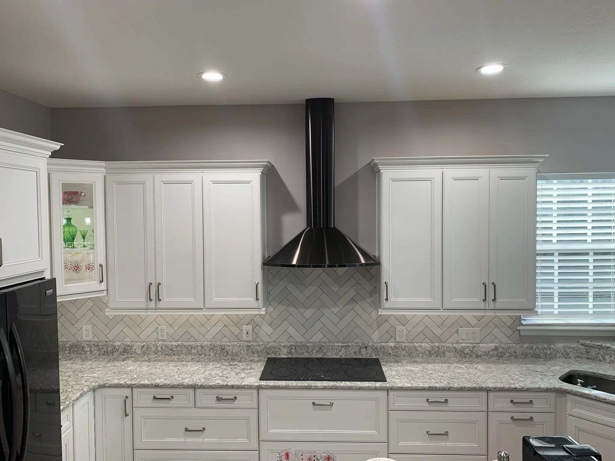 Wide white kitchen with a marble-look herringbone backsplash beneath the cabinets.