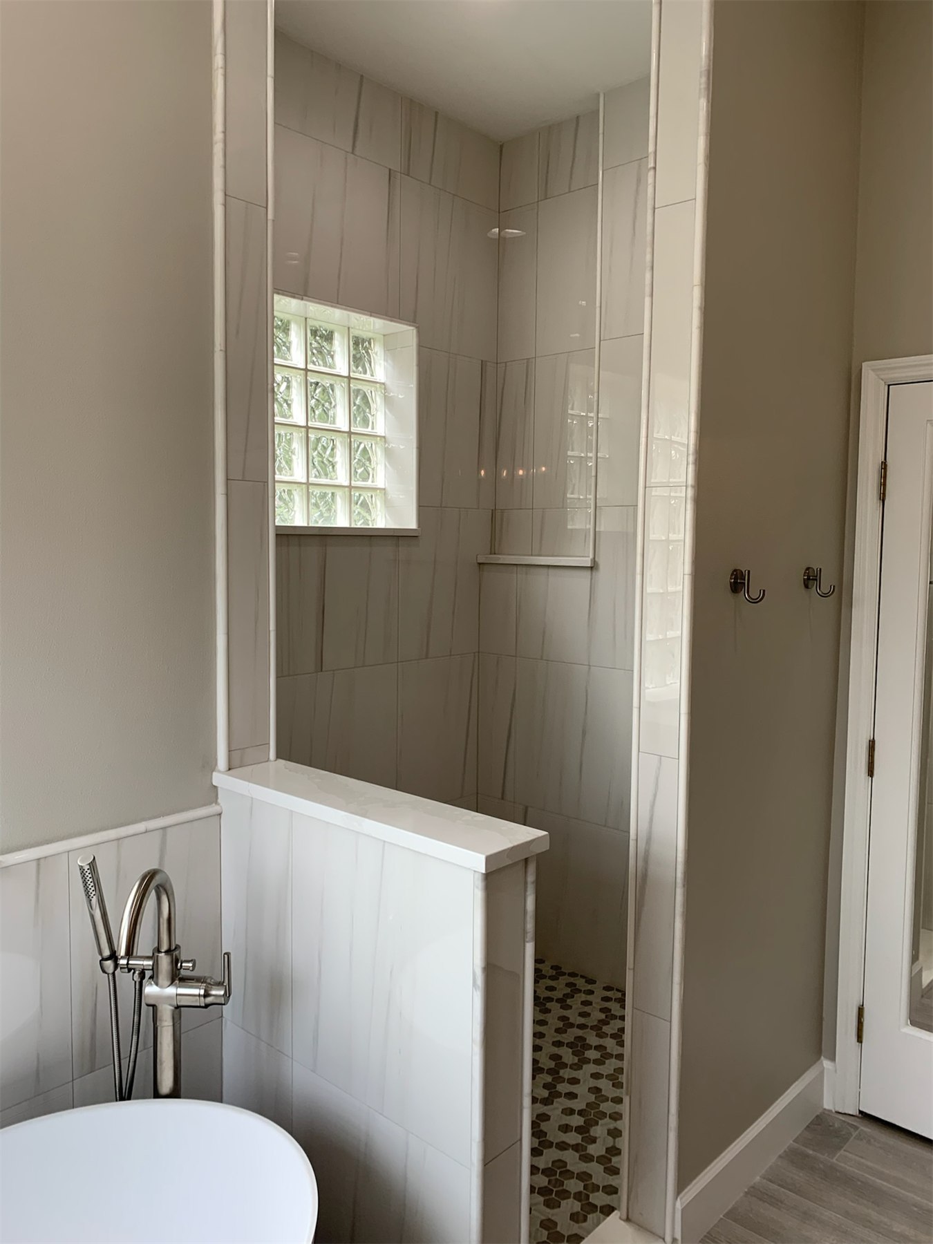 Walk-in shower with marble-look wall tile, pebble mosaic floor, recessed niche, and glass block window.