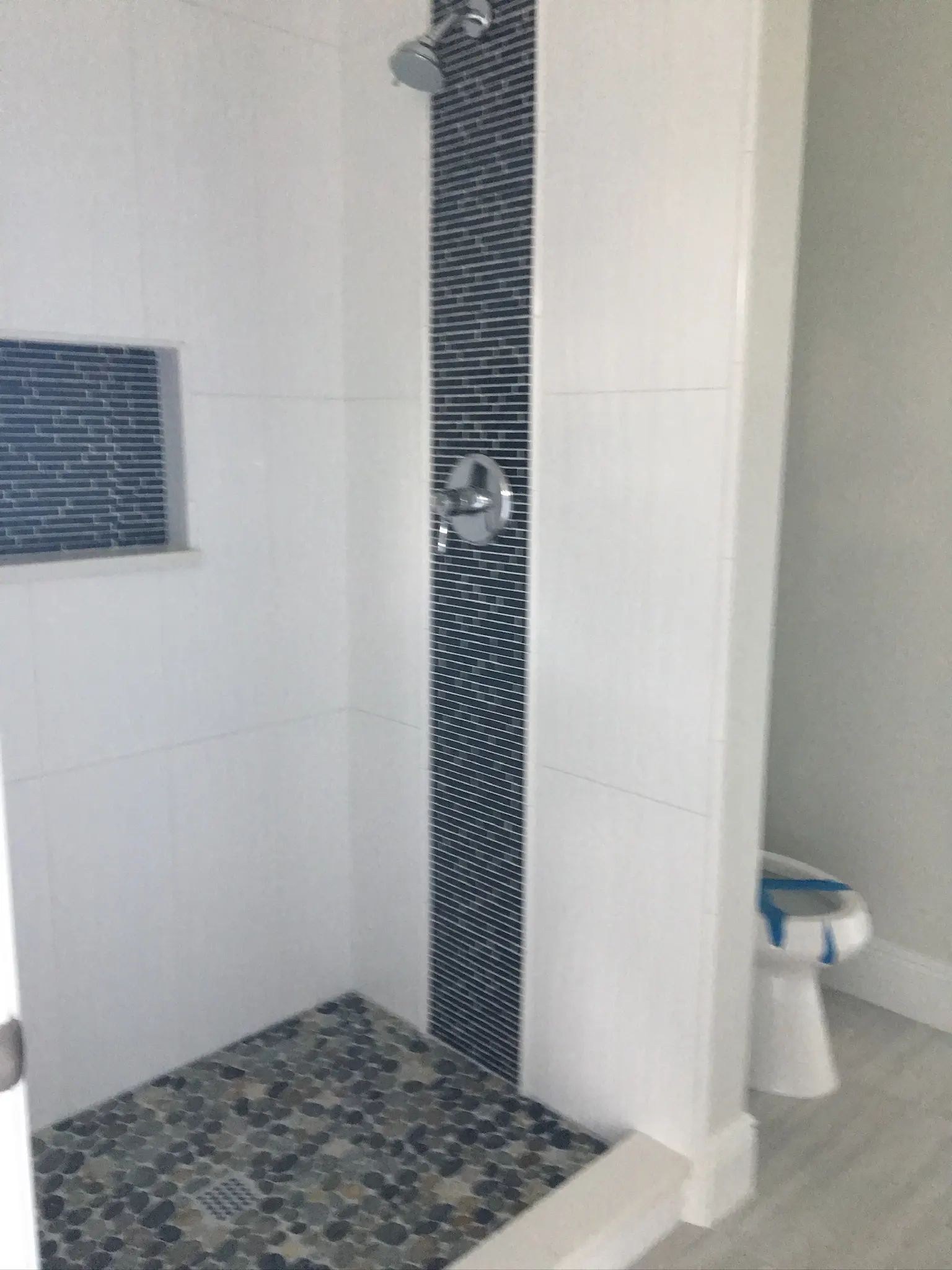 Angled view of a white tiled shower with a narrow vertical blue mosaic accent.
