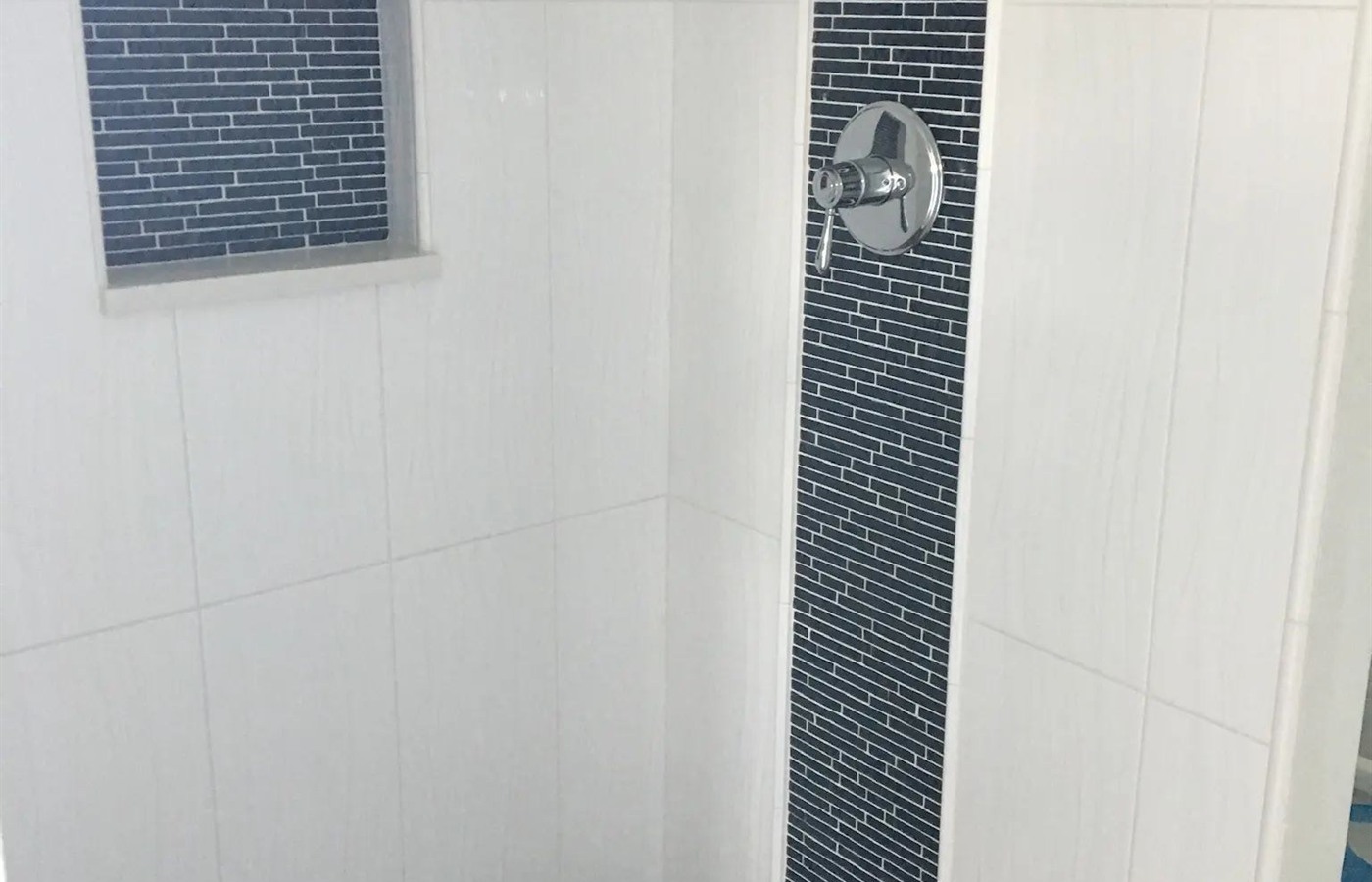 White shower with a vertical blue glass mosaic stripe, framed niche, and pebble floor.