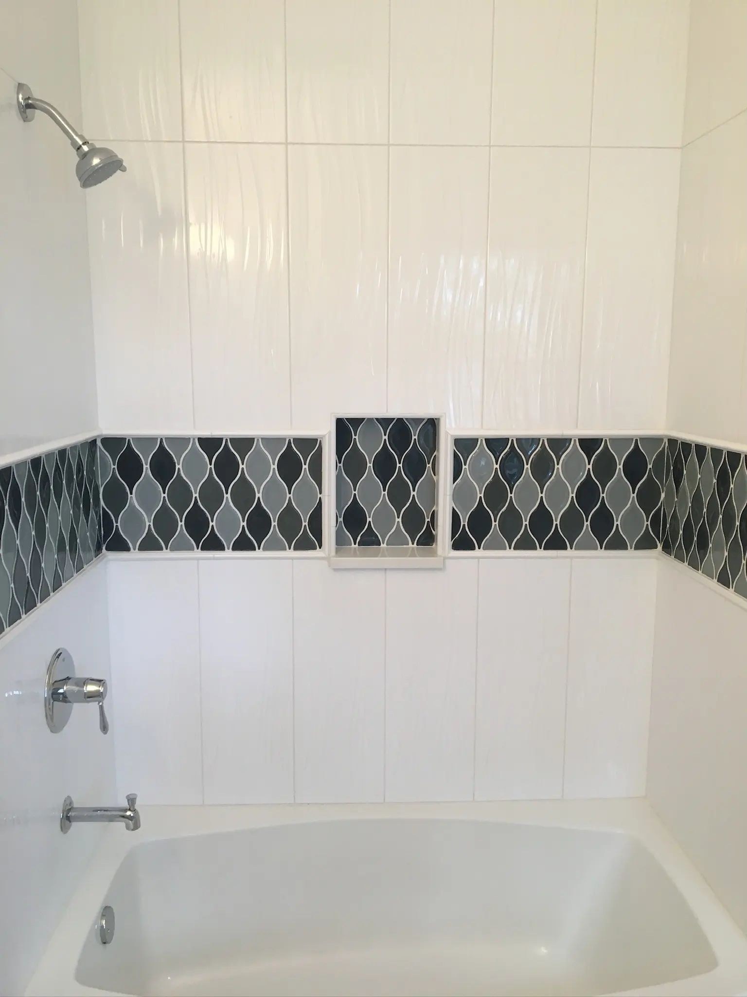 Straight-on view of a white tub surround with a continuous diamond mosaic accent stripe.