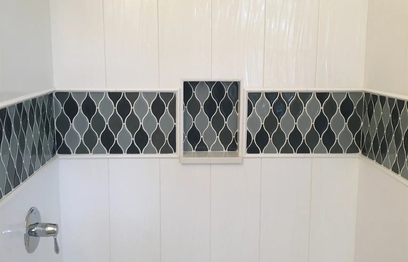 White tub surround with a dark diamond mosaic accent band and framed niche.