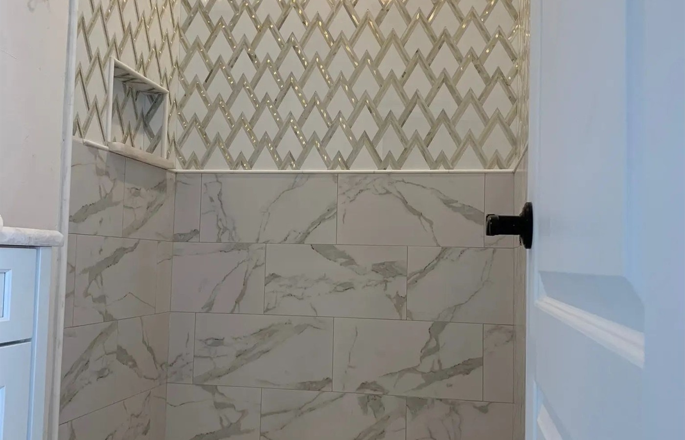 Geometric mosaic shower with marble-look wall tile and a pebble mosaic floor.