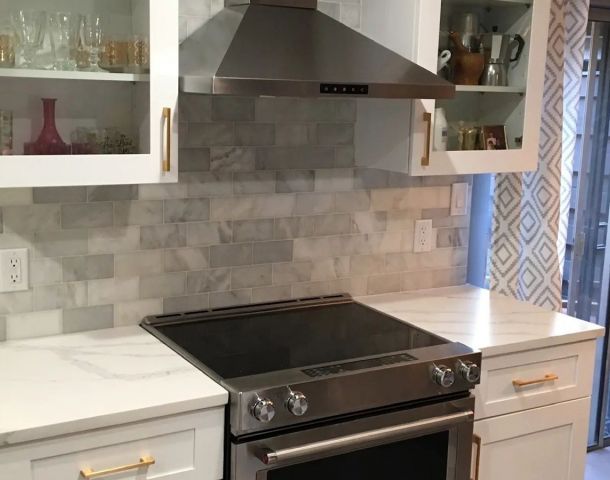 Bright white kitchen with a soft gray marble-look tile backsplash behind the range.