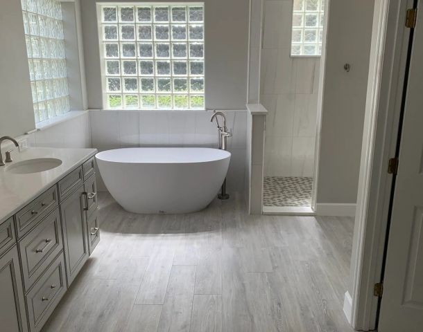 Modern bathroom with glass block windows, freestanding tub, gray vanity, and tiled shower.