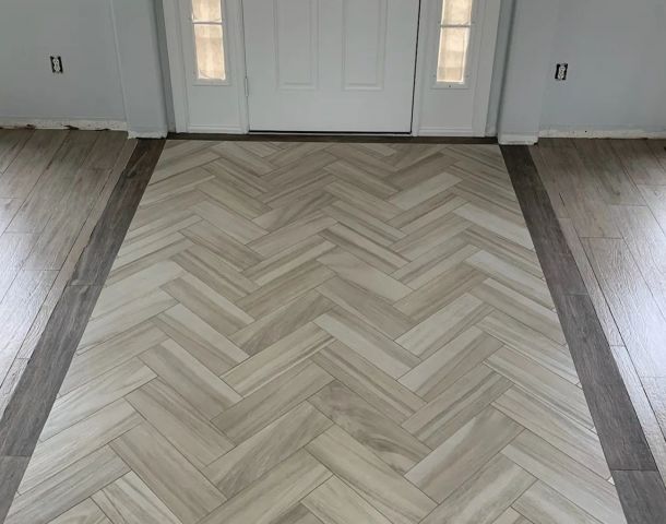 Herringbone tile entry inset framed by a dark border and wood-look plank flooring.