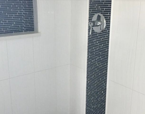 White shower with a vertical blue glass mosaic stripe, framed niche, and pebble floor.