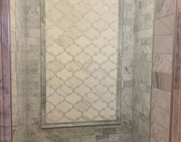 Gray marble shower with a framed patterned accent panel and stone bench.